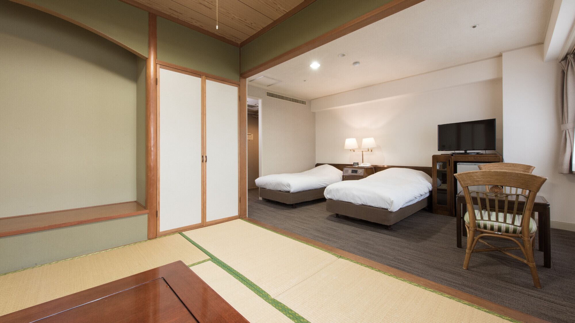 Habitación de hotel con dos camas, televisión, escritorio con silla y puerta corredera tradicional japonesa.