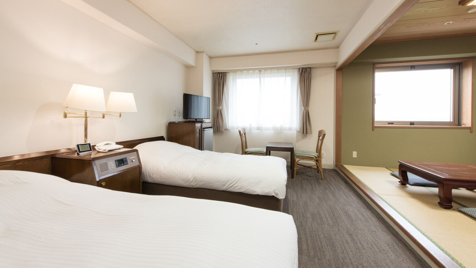 A hotel room with two beds, a TV, a desk, a chair, and a futon.