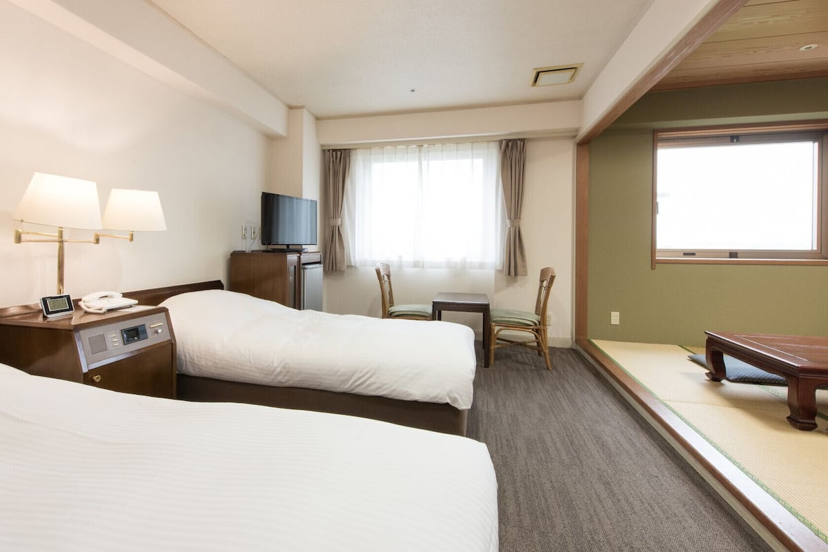 A hotel room with two beds, a TV, a desk, a chair, and a futon.
