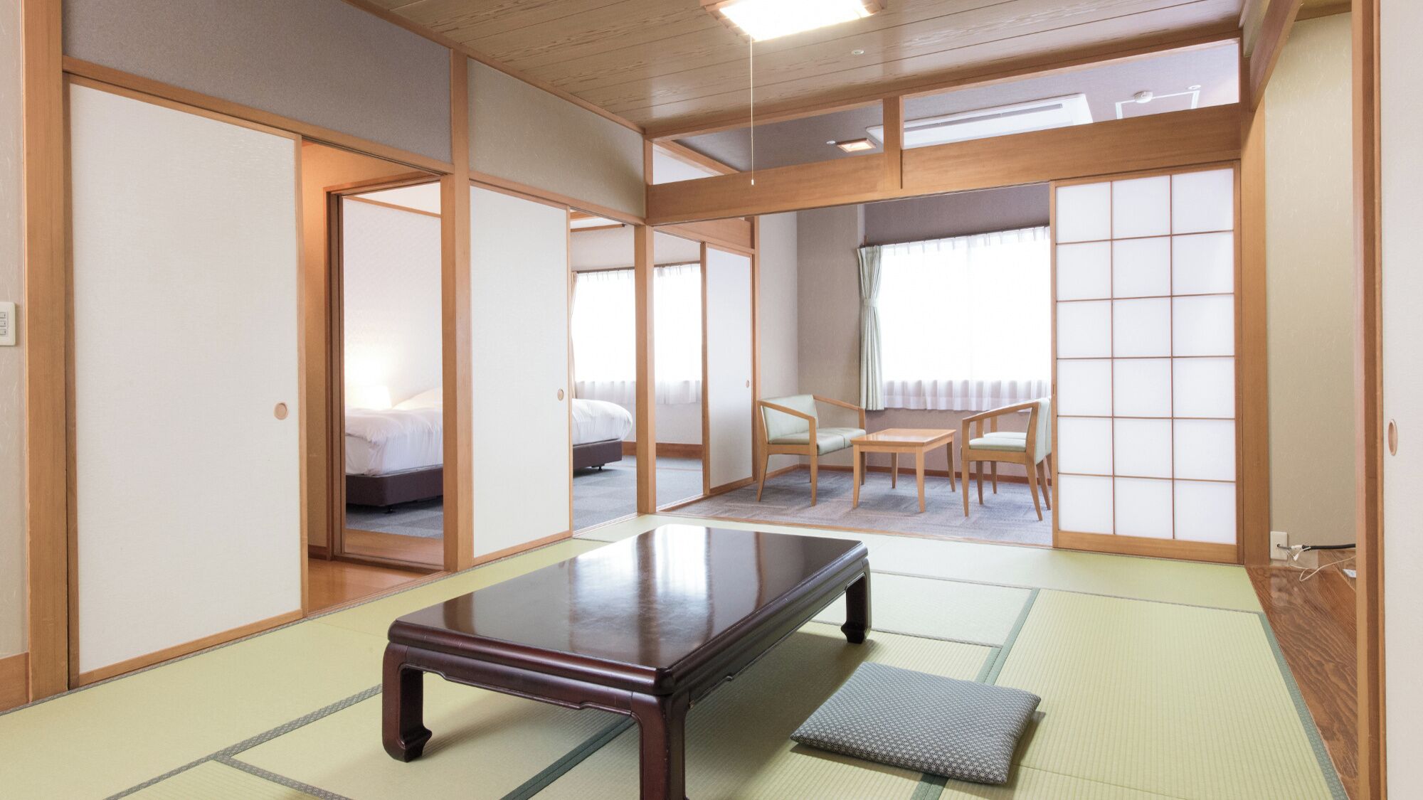 A traditional Japanese room with tatami flooring, a low table, sliding doors, and a bed in the background.