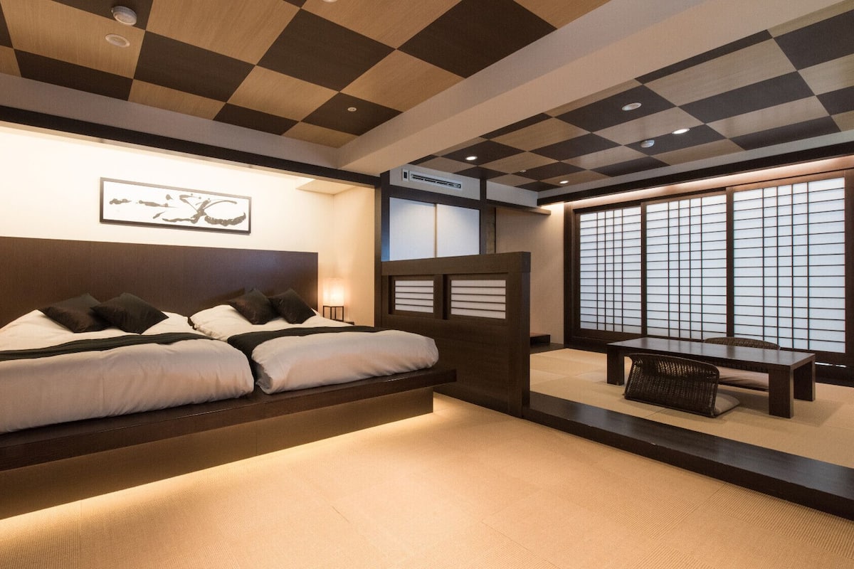 A modern hotel room with a large bed, bedside lamps, a wall-mounted air conditioner, and a view through a shoji screen.