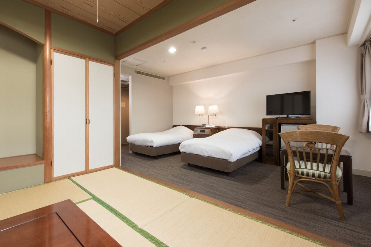 A hotel room with two beds, a TV, a desk, and a chair.