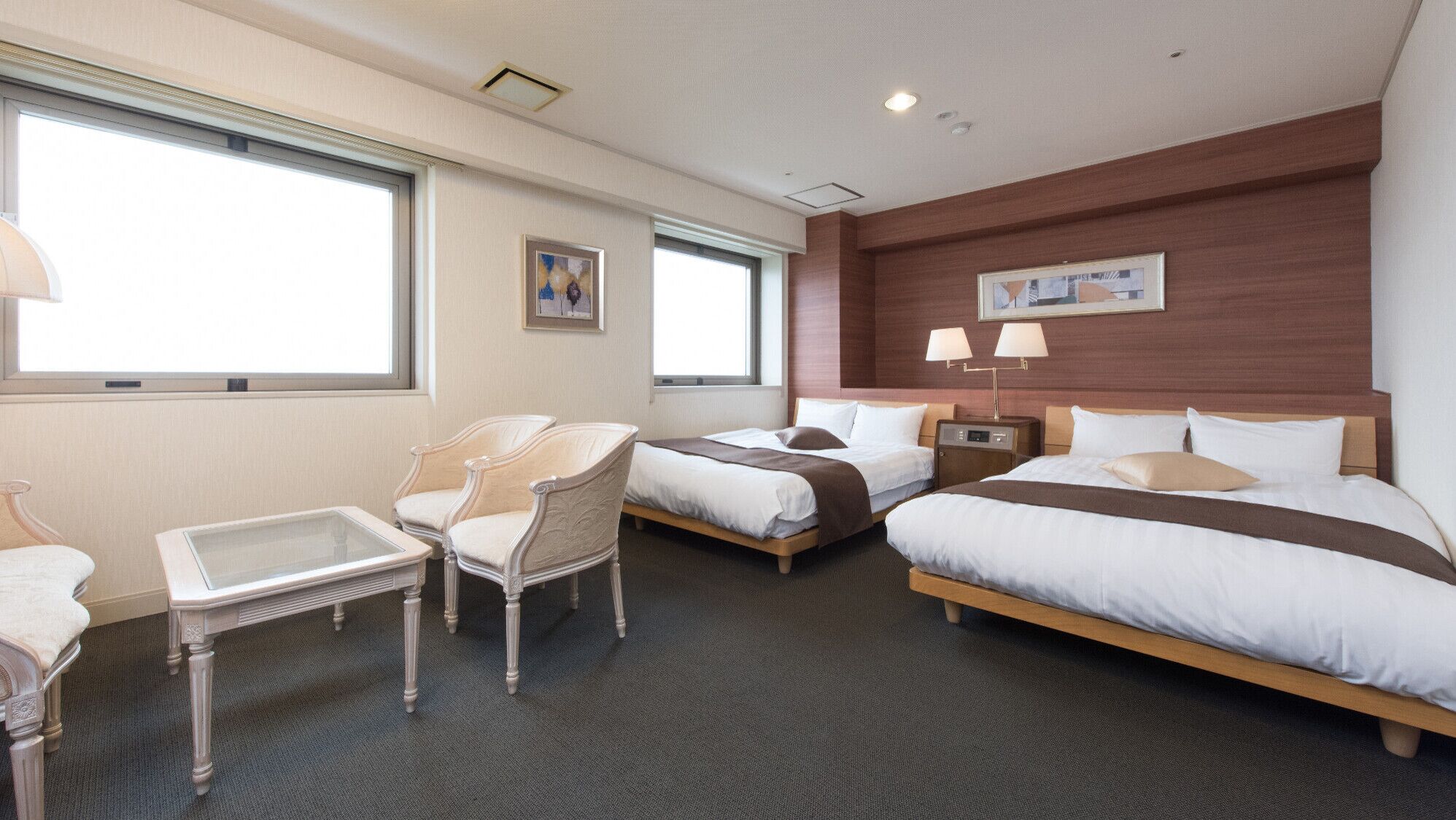 A hotel room with two beds, a desk, a chair, and two bedside lamps.