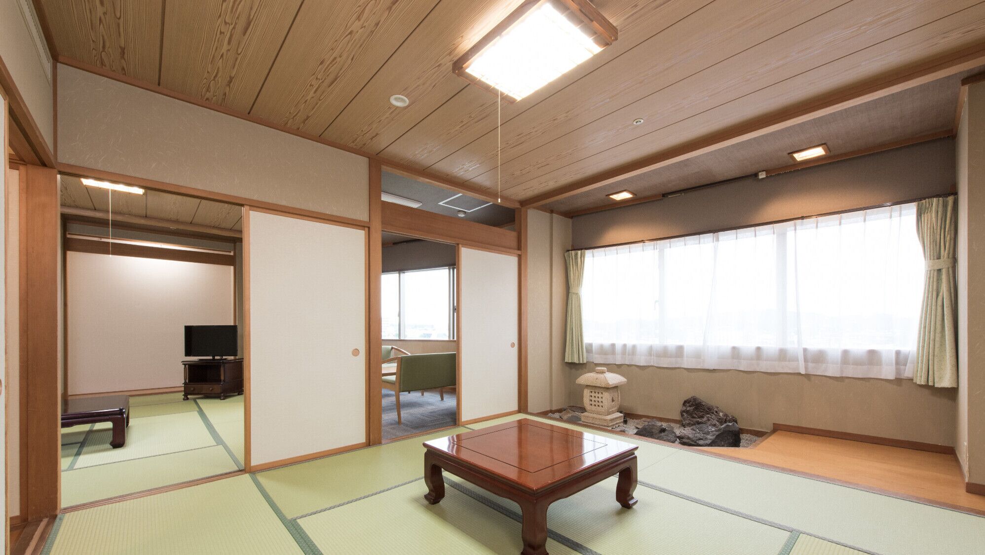 A traditional Japanese room with tatami flooring, a low wooden table, sliding doors, and a television in the corner.