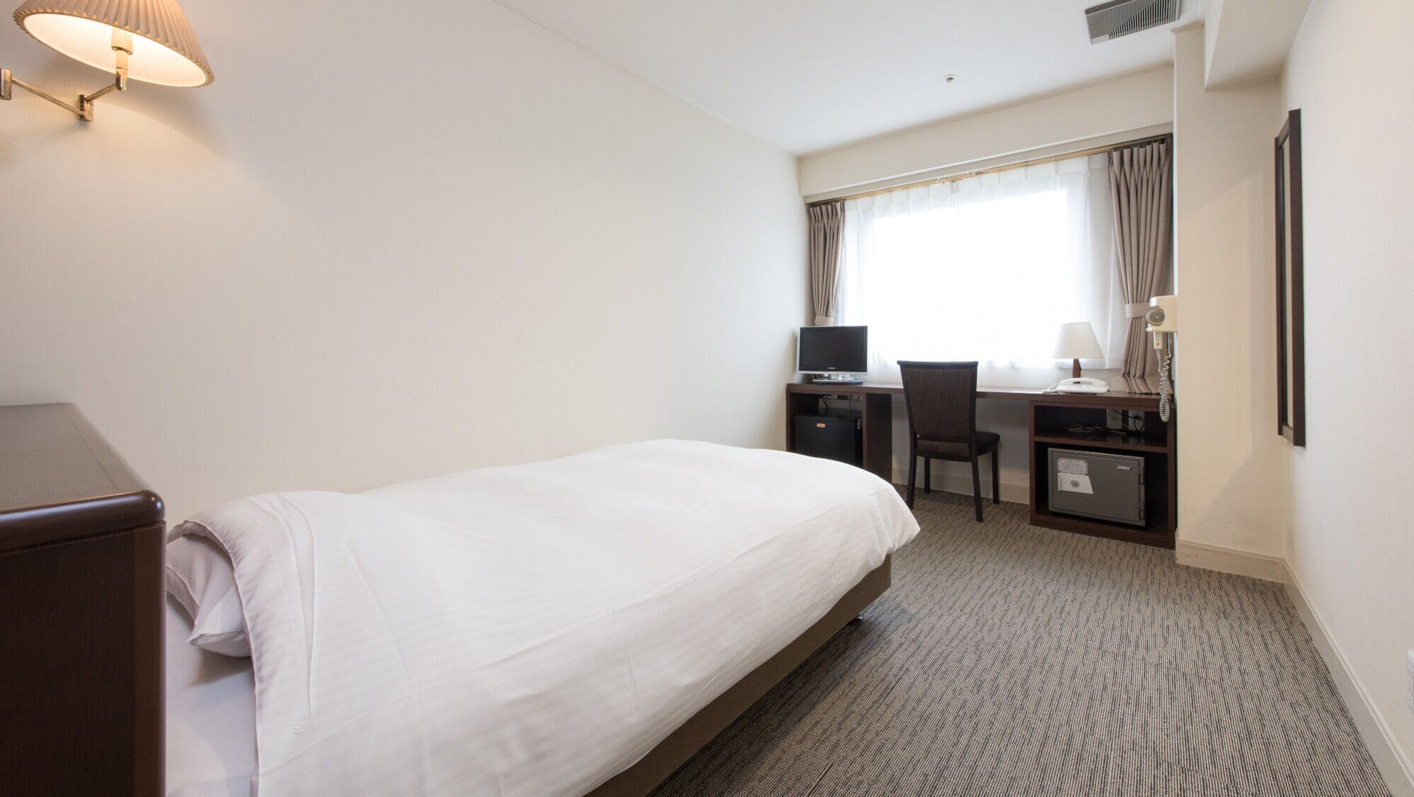 A hotel room with a bed, desk, chair, and a window with curtains.
