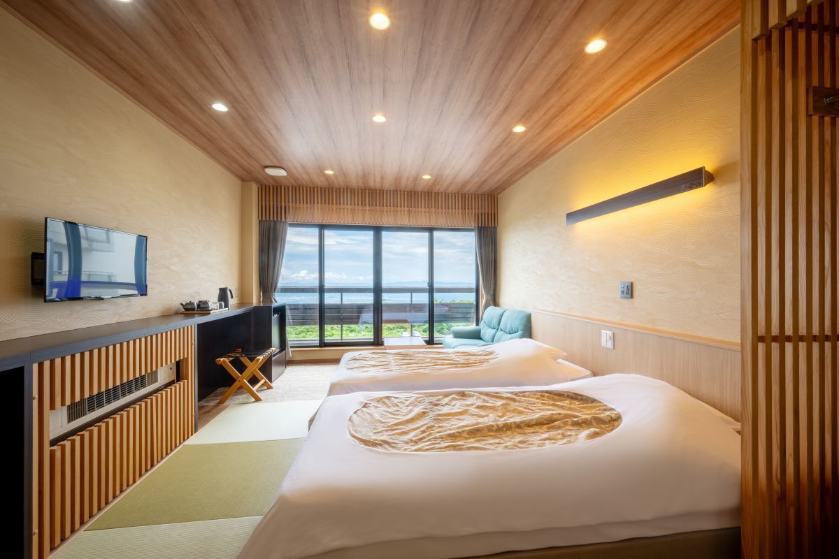 A hotel room with two beds, a TV, a desk, and a large window with a view.