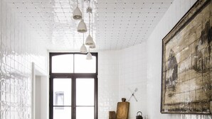 A dining area with white tiled walls, a large window, and a rustic fireplace. - La Maison Haute Guest House (Brussels)