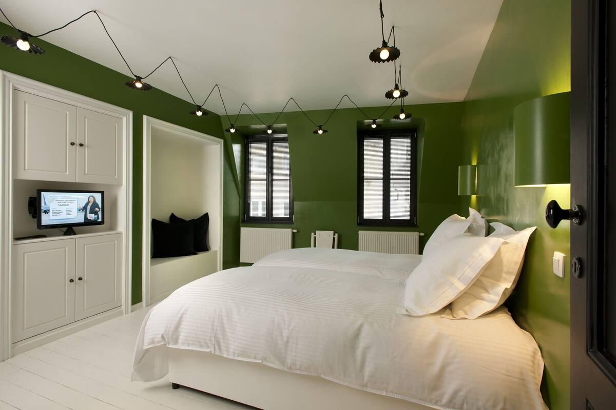 A bedroom with a large bed, white cabinets, a television, and green walls.