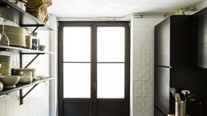 A narrow kitchen with a wooden countertop, shelves with kitchenware, a black door, and a hanging light fixture. - La Maison Haute Guest House (Brussels)