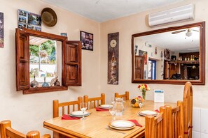 Un coin repas avec une table en bois dressée pour quatre personnes, entourée de chaises en bois. Un grand miroir reflète la pièce, et une horloge au mur indique l’heure.