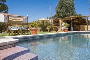 Un espace piscine avec une bordure carrelée, des chaises longues et une pergola dotée d’un auvent.