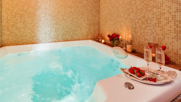 A bathtub with a tray of strawberries and champagne glasses, surrounded by candles and flowers. - Dimora Soleda (Ugento)