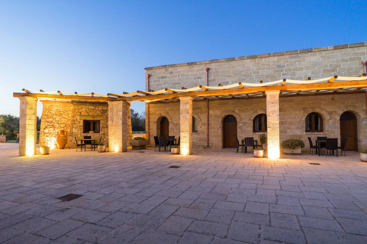 Area patio esterna con pavimento in pietra, pergola in legno e zone relax.