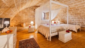 A bedroom with a four-poster bed, wooden floors, stone walls, and a television on a dresser. - Dimora Soleda (Ugento)
