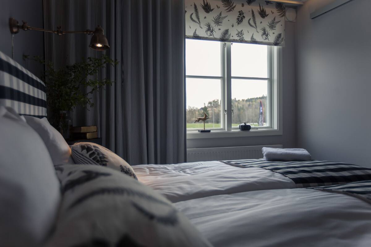 A bedroom with a large window, a bedside lamp, and a view of the outdoors.