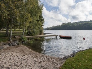 A lakeside scene with a dock, a boat, and a sandy beach.