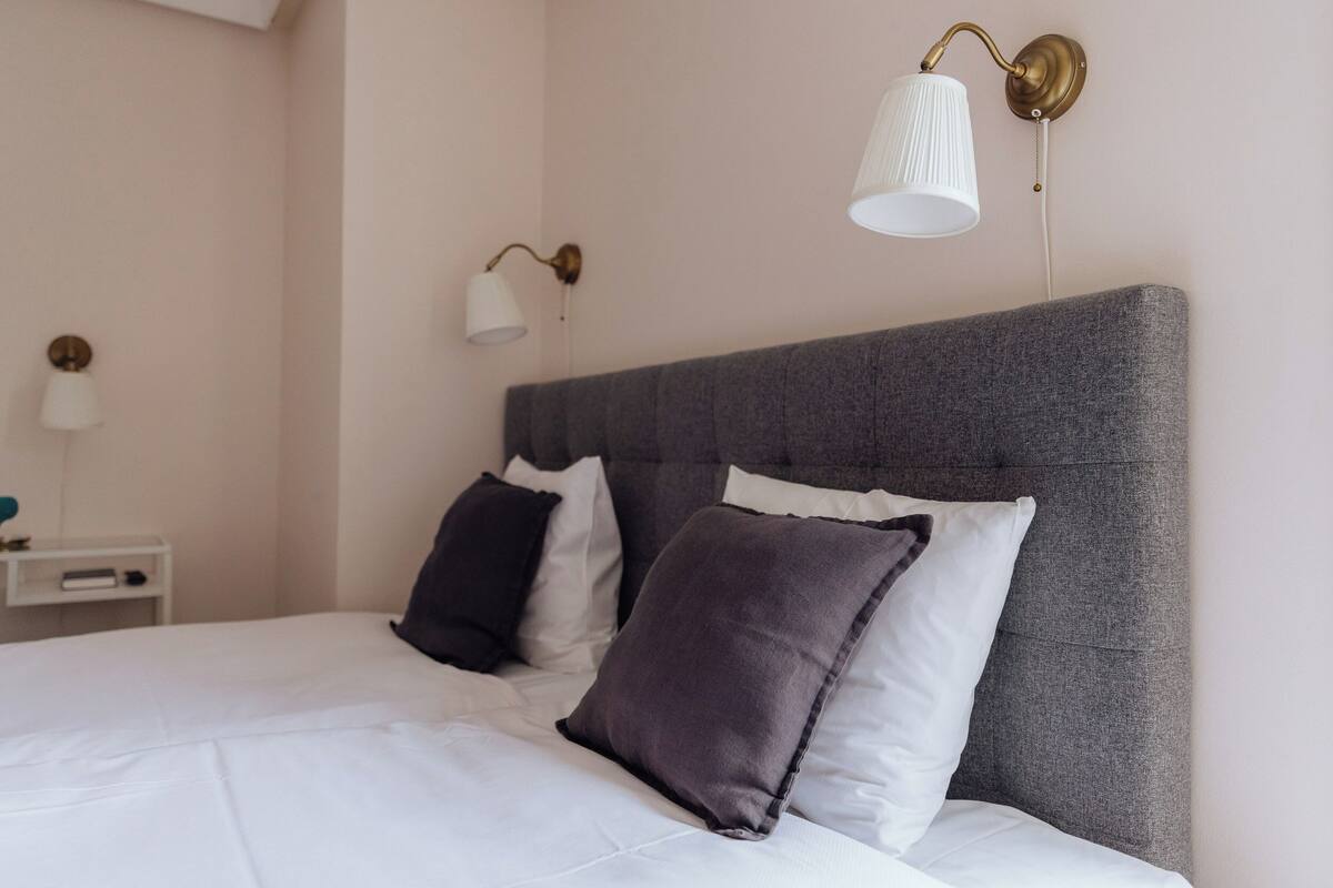 A neatly made bed with a grey headboard, white bedding, and two bedside lamps.