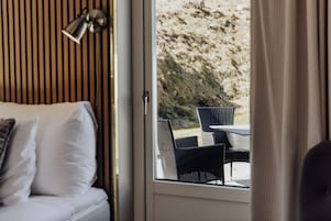 Una habitación con cama, ventana y zona de estar exterior con sillas.