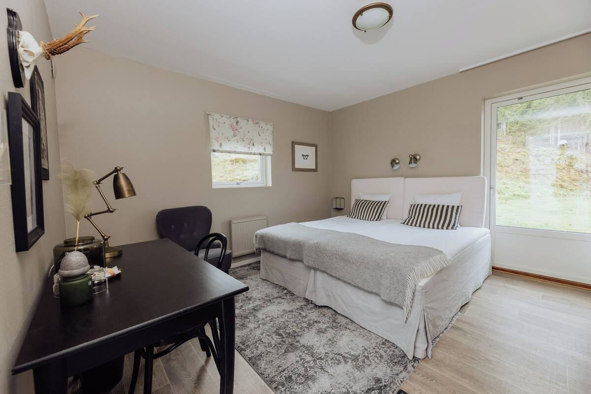 A bedroom with a bed, a desk, a chair, a window, and a radiator.