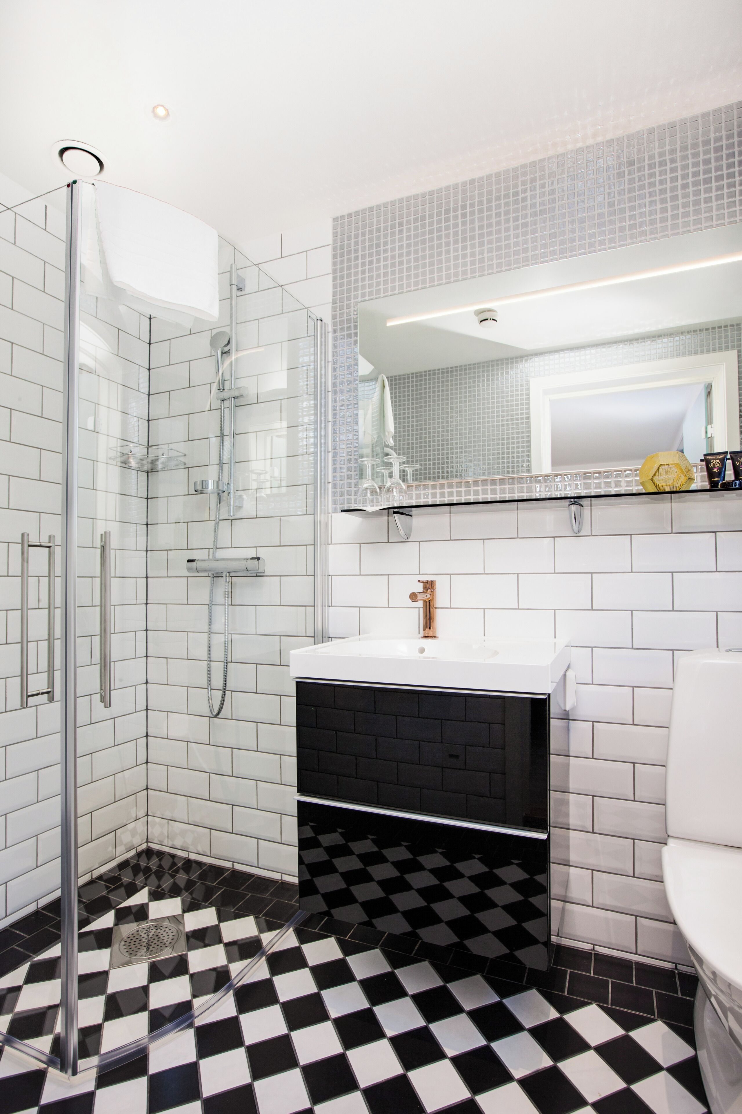 A bathroom with a glass-enclosed shower, a white sink with a black vanity, and a checkered floor pattern.