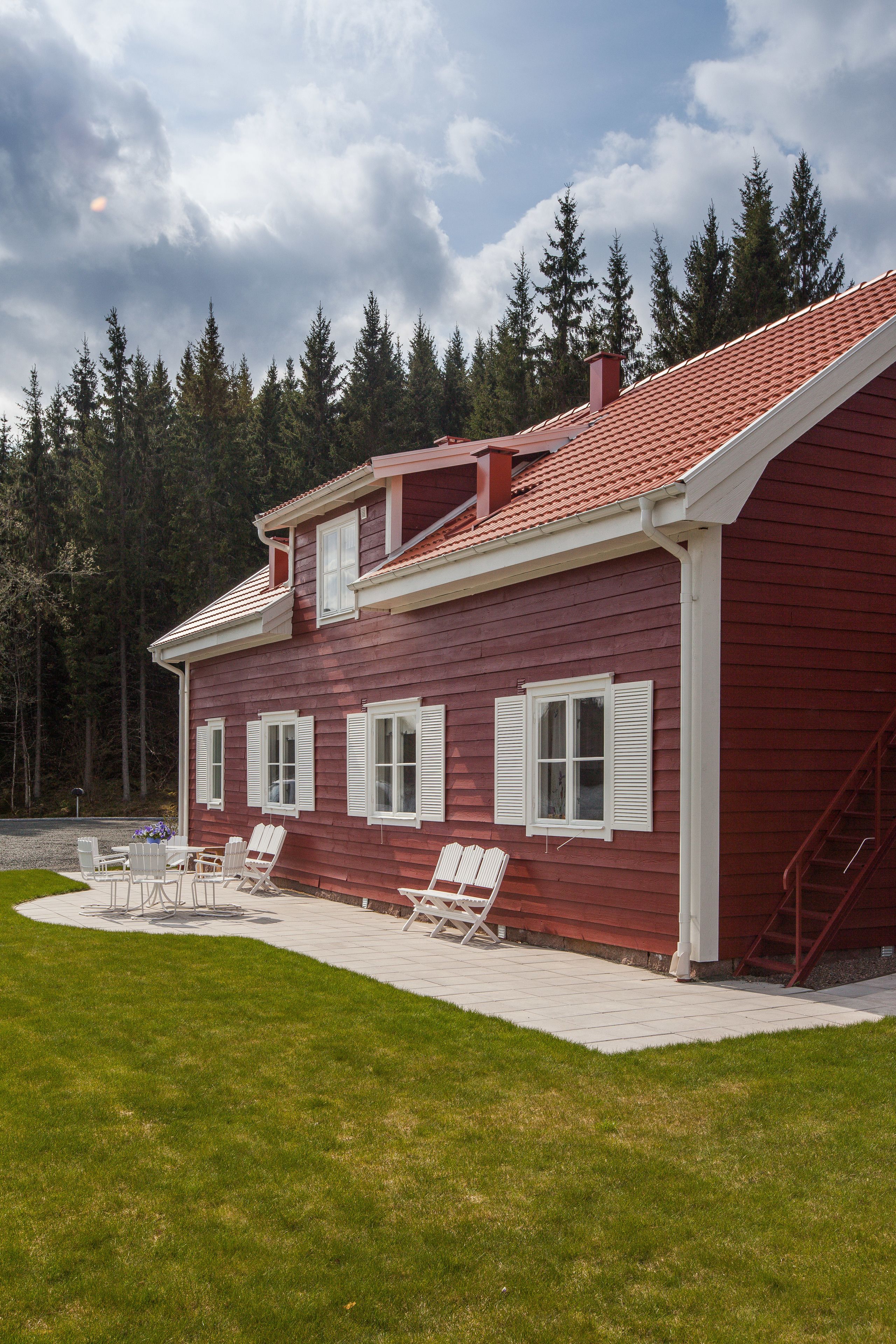 A two-story house with a red exterior and white trim, featuring a covered patio with outdoor furniture.