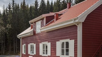 A two-story house with a red exterior and white trim, featuring a covered patio with outdoor furniture.
