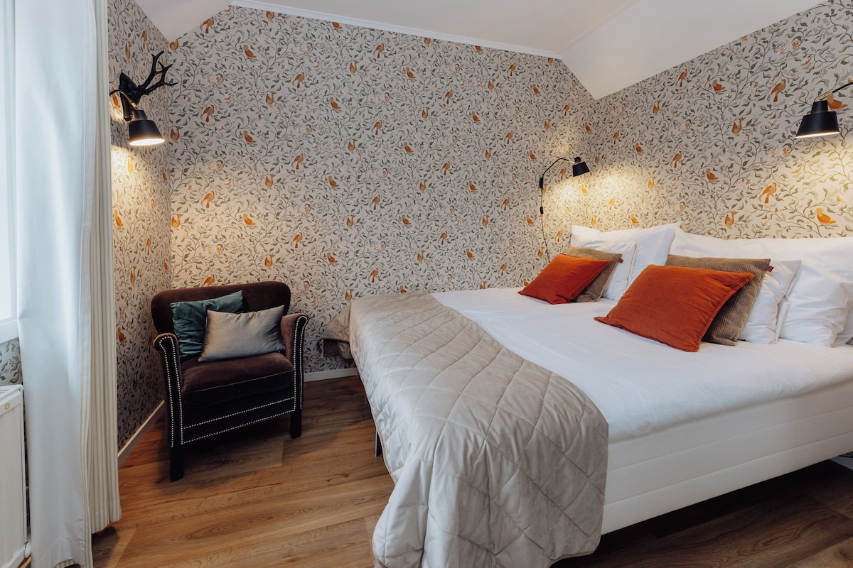 Ein Schlafzimmer mit einem großen Bett, einem Sessel und Wandtapete mit Muster.
