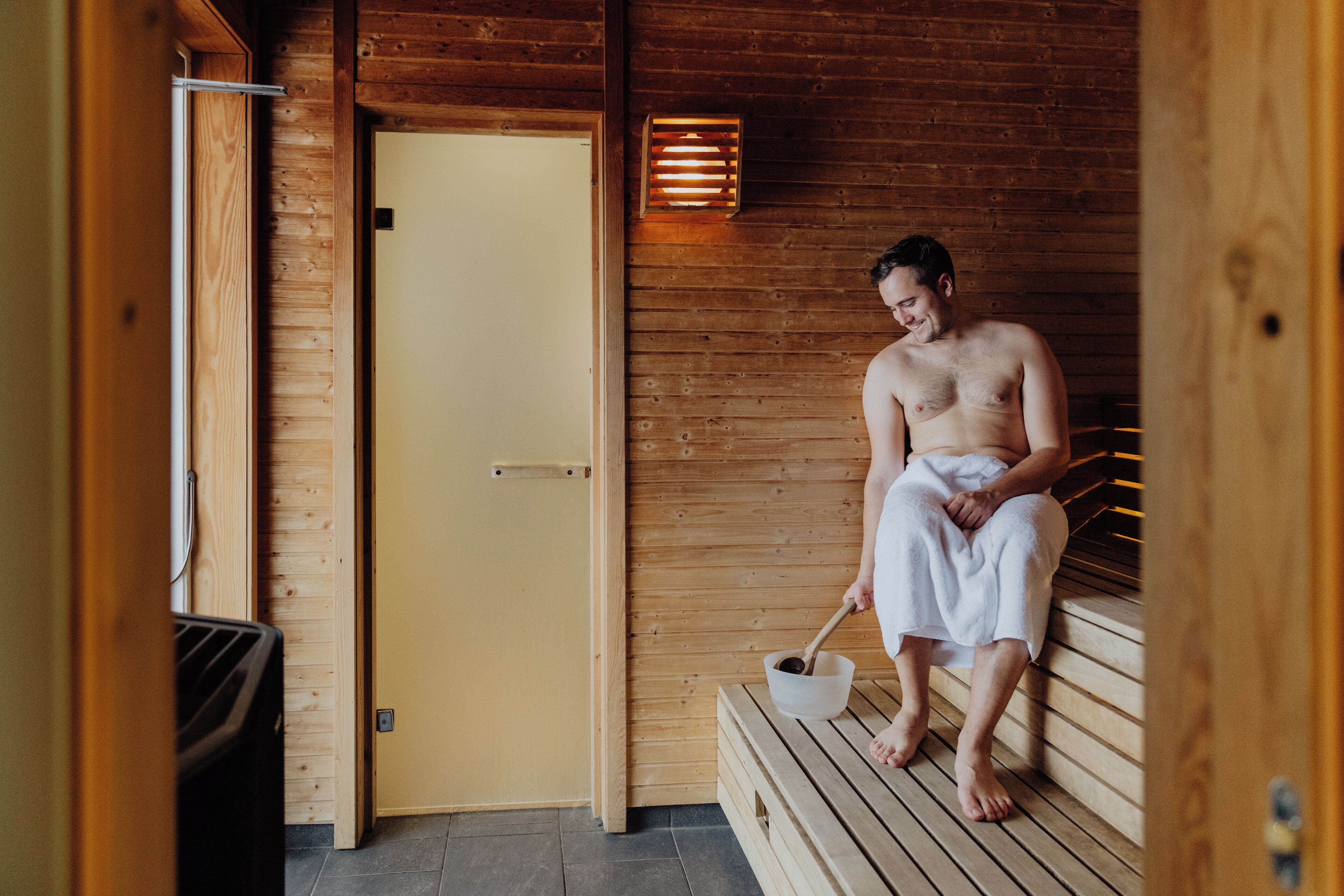Una sauna de madera con un banco, una puerta y una lámpara fijada a la pared.