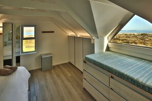 A bedroom with a large window, a bed with a patterned mattress, a bedside table, and a wardrobe.