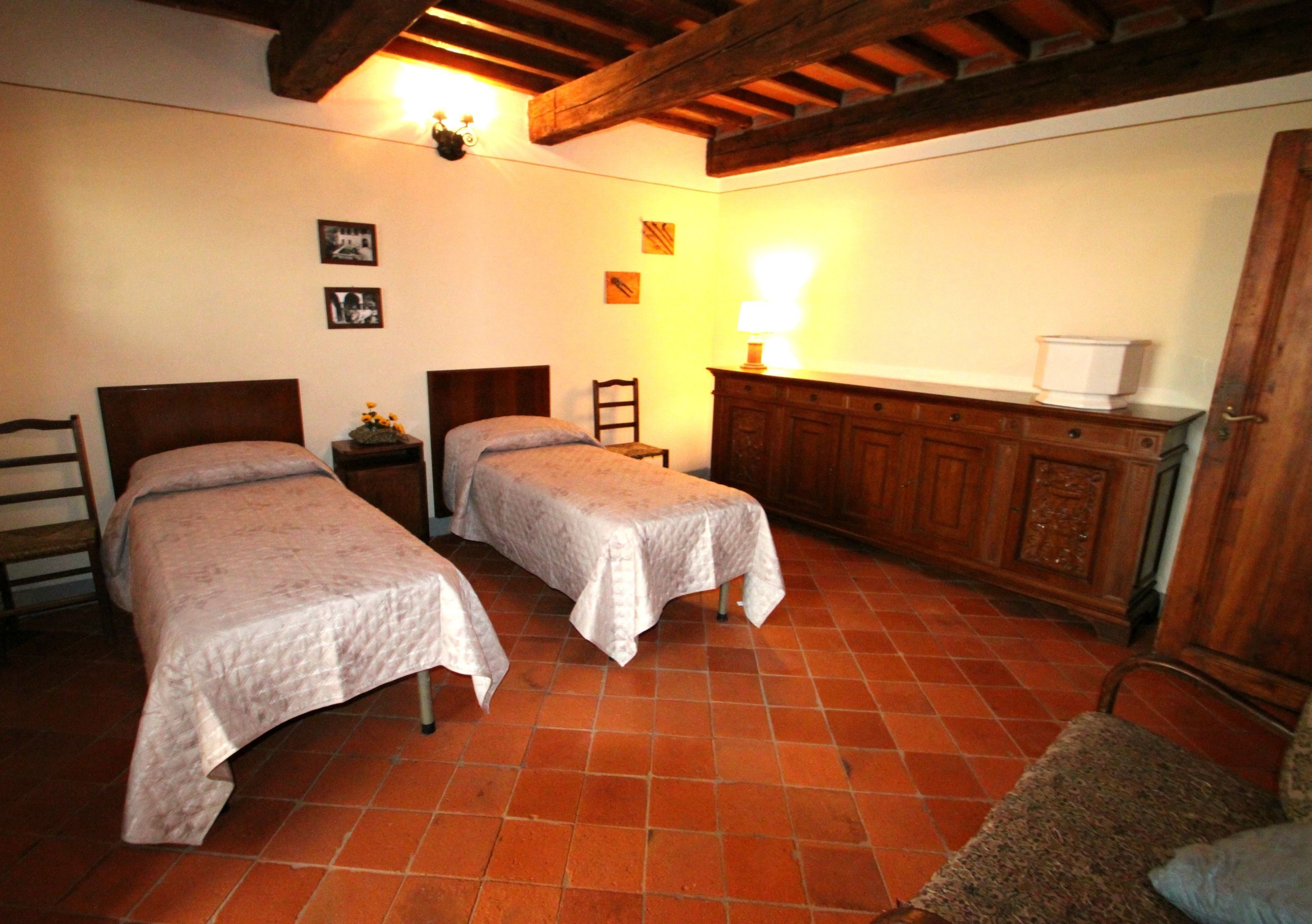A bedroom with two single beds, a wooden cabinet, a chair, and a small table with a lamp.