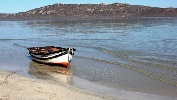 Ein Boot an einem sandigen Strand, im Hintergrund ein felsiger Hügel.