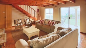 Ein geräumiges Wohnzimmer mit einer Holztreppe, einem weißen Sofa, einem beigefarbenen Sofa und einem Couchtisch.