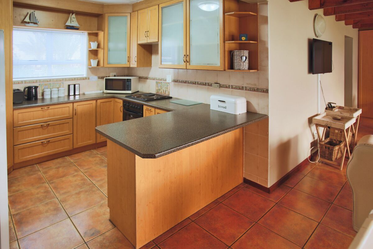 A kitchen with wooden cabinets, a central island, a microwave, and a bread box.