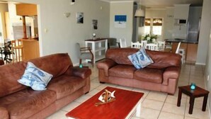 A living room with two brown leather sofas, a wooden coffee table, and a small side table. - 6 Nendaz Self catering (Langebaan)
