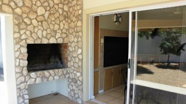 A stone wall with a flat-screen TV mounted on it, a sliding glass door leading to an outdoor area, and a tiled floor. - 6 Nendaz Self catering (Langebaan)