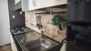 A modern kitchen with a stone backsplash, stainless steel appliances, and a hanging utensil rack. - Italianway   - San Gottardo (Milan)