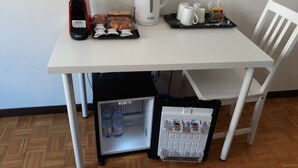 Une petite cuisine équipée d’une machine à café, d’une bouilloire et d’un mini-réfrigérateur contenant des bouteilles d’eau et des en-cas.