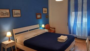 A bedroom with a bed, a nightstand, a chair, and a window with curtains.