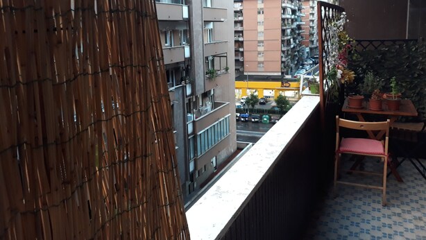 Un balcon offrant une vue sur le paysage urbain, avec notamment un immeuble à plusieurs étages et une devanture de magasin jaune.