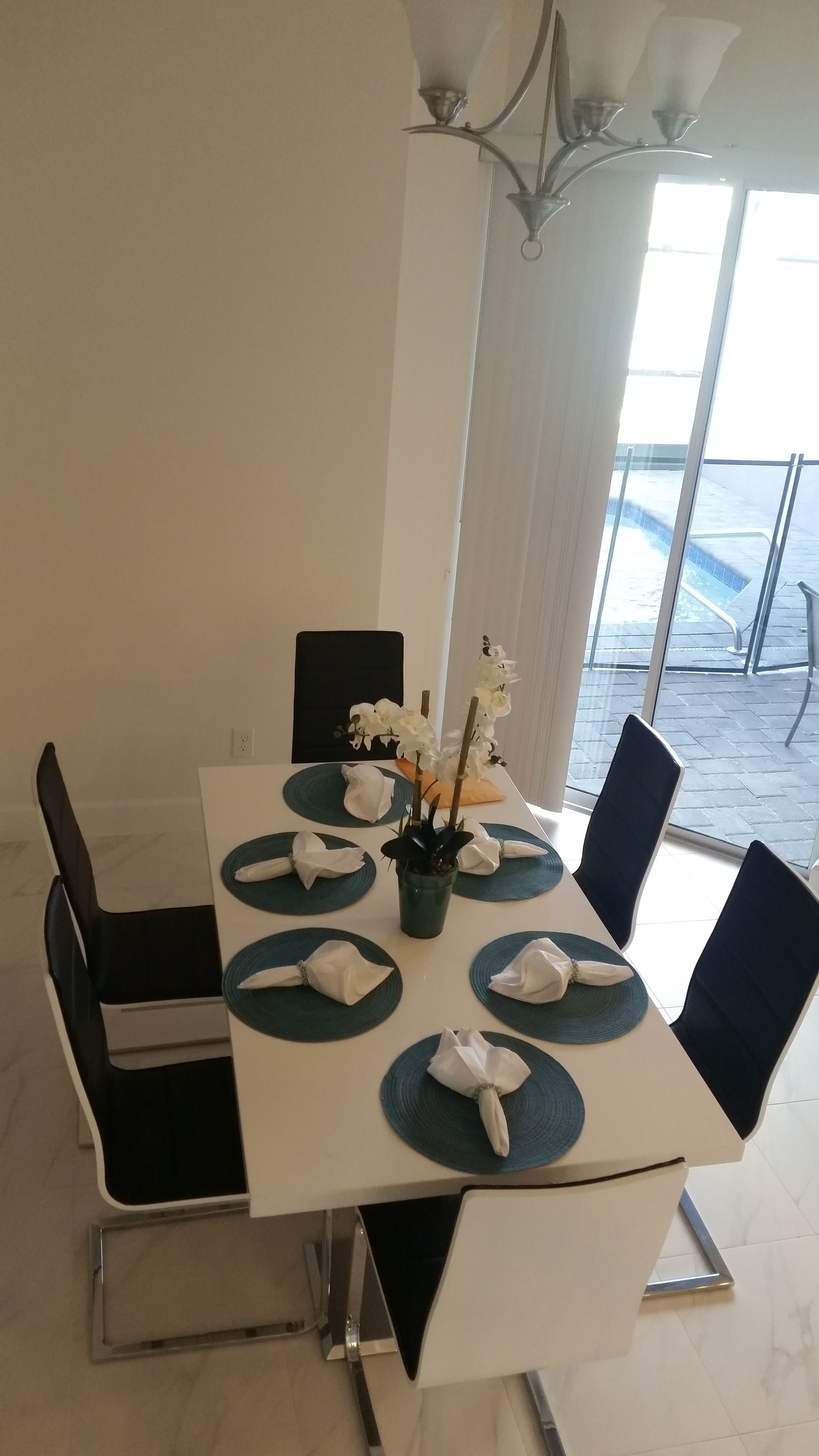 Une table à manger dressée avec des serviettes blanches, des sets de table bleus et un vase rempli de fleurs blanches.