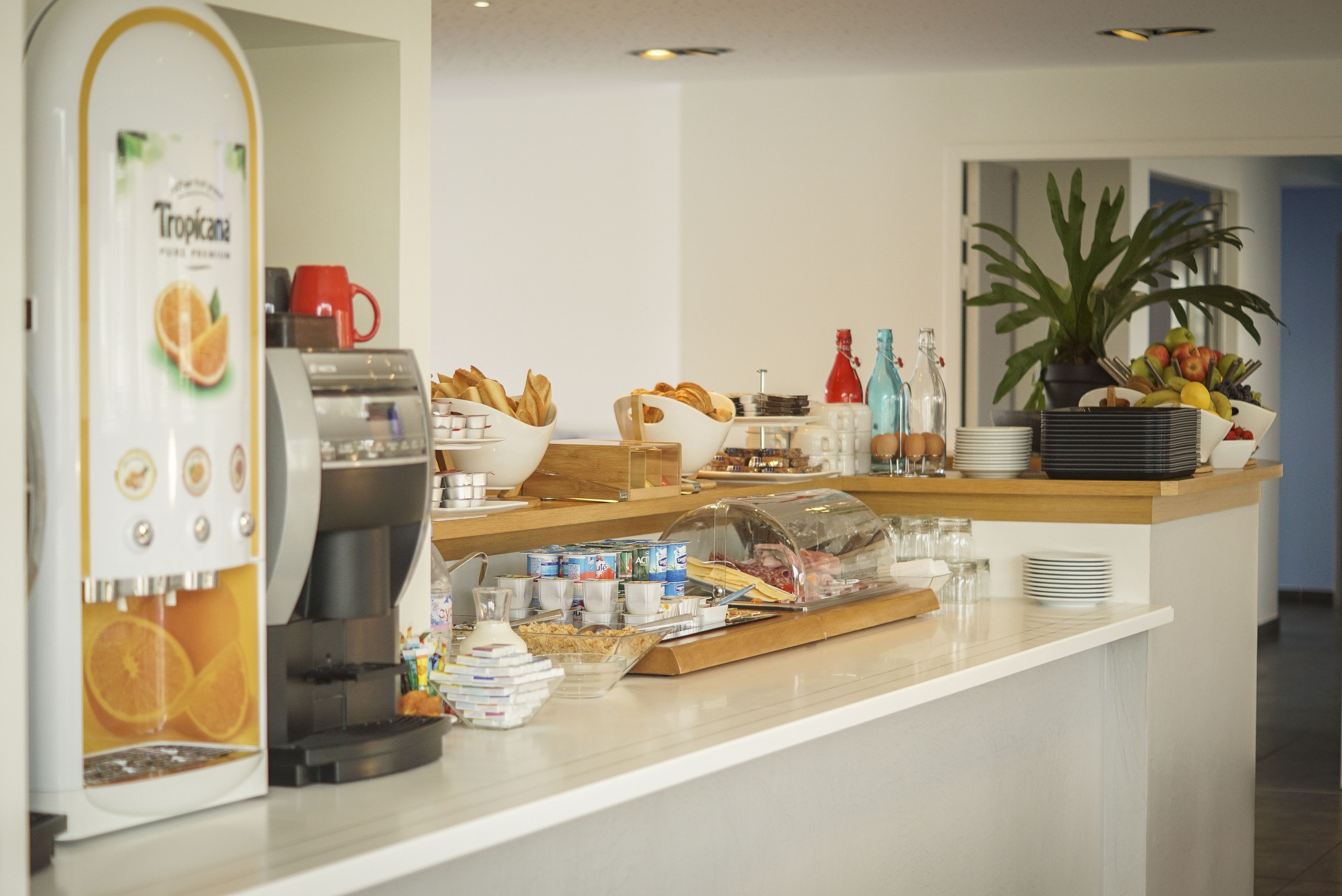 A breakfast buffet area with a coffee machine, bread, fruits, and condiments.
