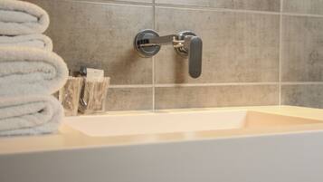 Une salle de bain avec un lavabo blanc, un porte-serviettes avec des serviettes pliées et un récipient en verre contenant des articles de toilette.