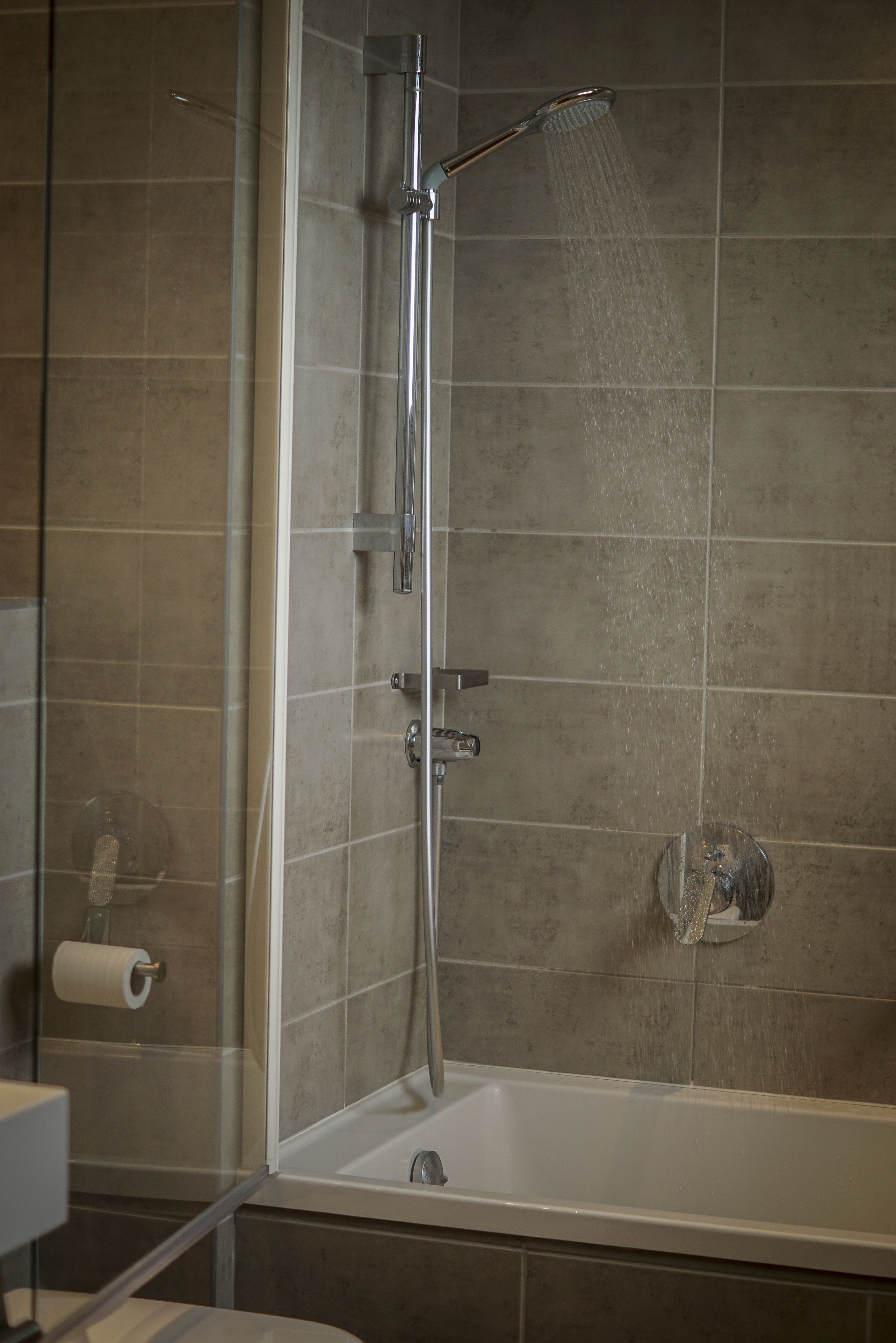 A shower with a glass door, a bathtub, and a toilet paper roll on the wall.