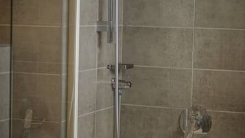 A shower with a glass door, a bathtub, and a toilet paper roll on the wall.