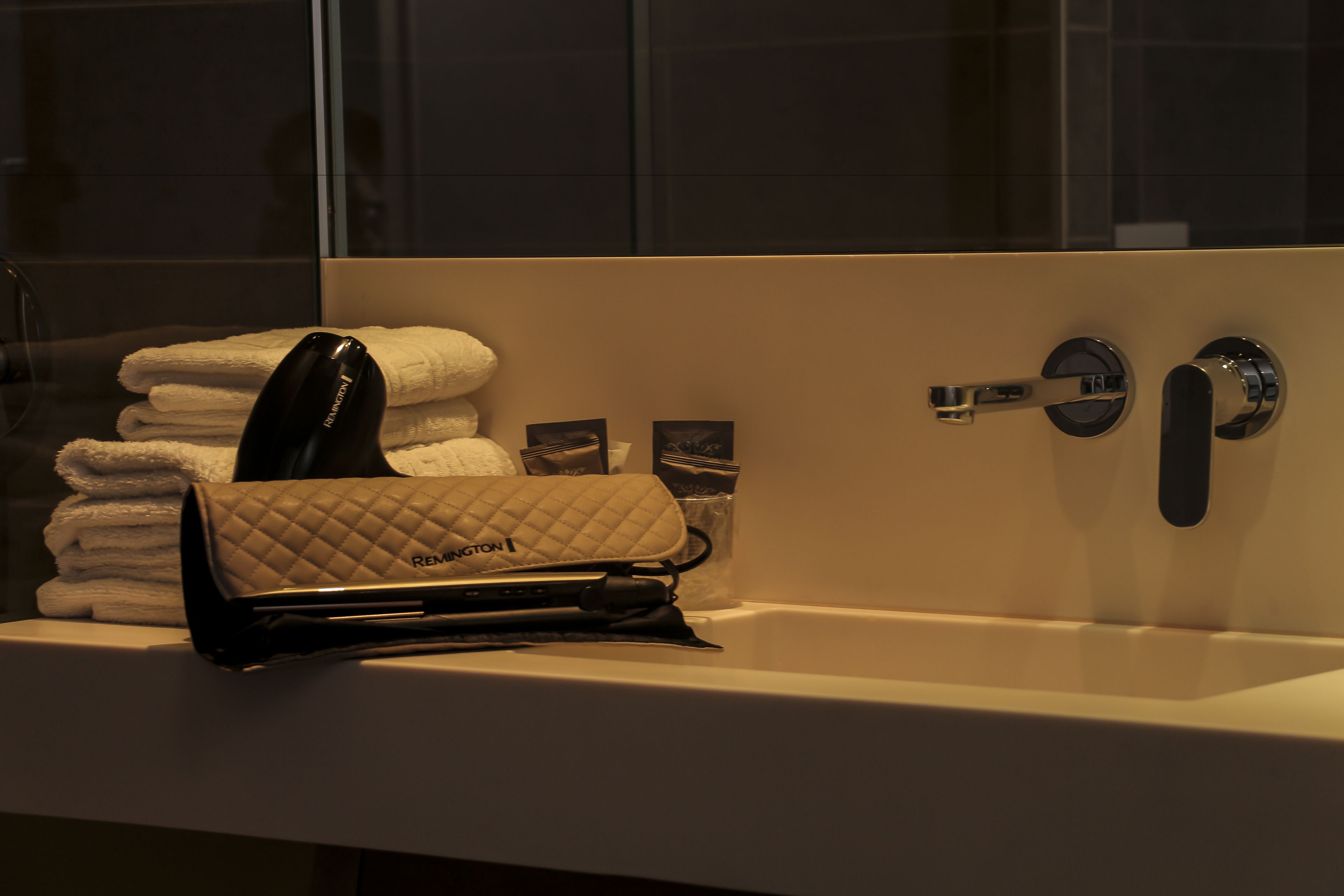 A bathroom with a sink, a towel rack with folded towels, and a quilted bag on the counter.