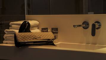 A bathroom with a sink, a towel rack with folded towels, and a quilted bag on the counter.