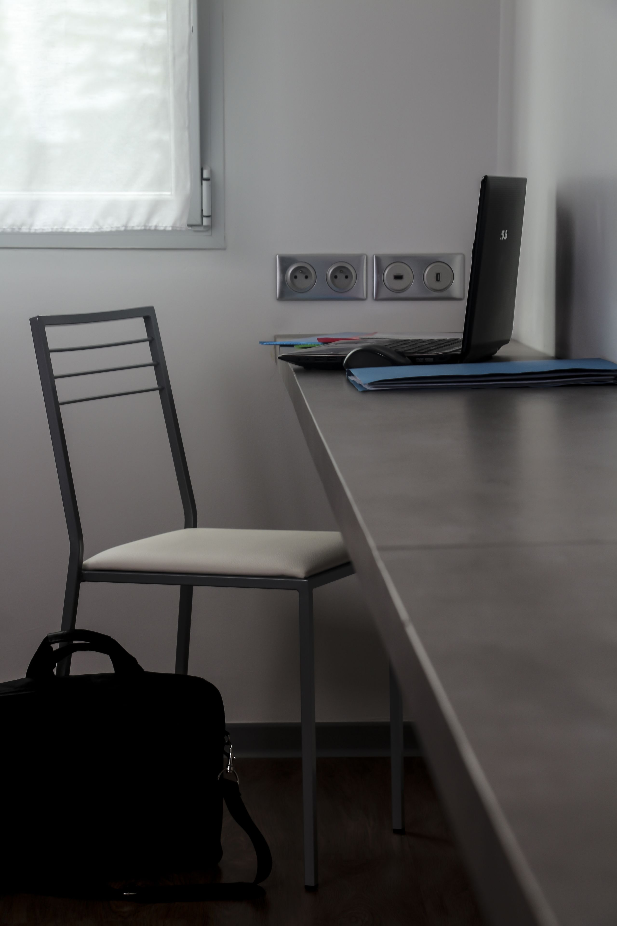 Un espacio de trabajo moderno con una computadora portátil sobre un escritorio, una silla y un bolso.