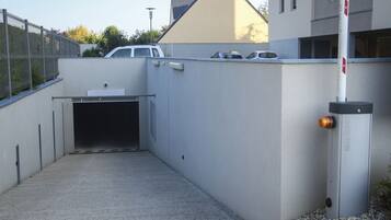 A parking garage entrance with a concrete floor, a metal fence, and a white building in the background.
