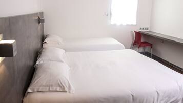 A hotel room with two beds, a red chair, and a window with blinds.