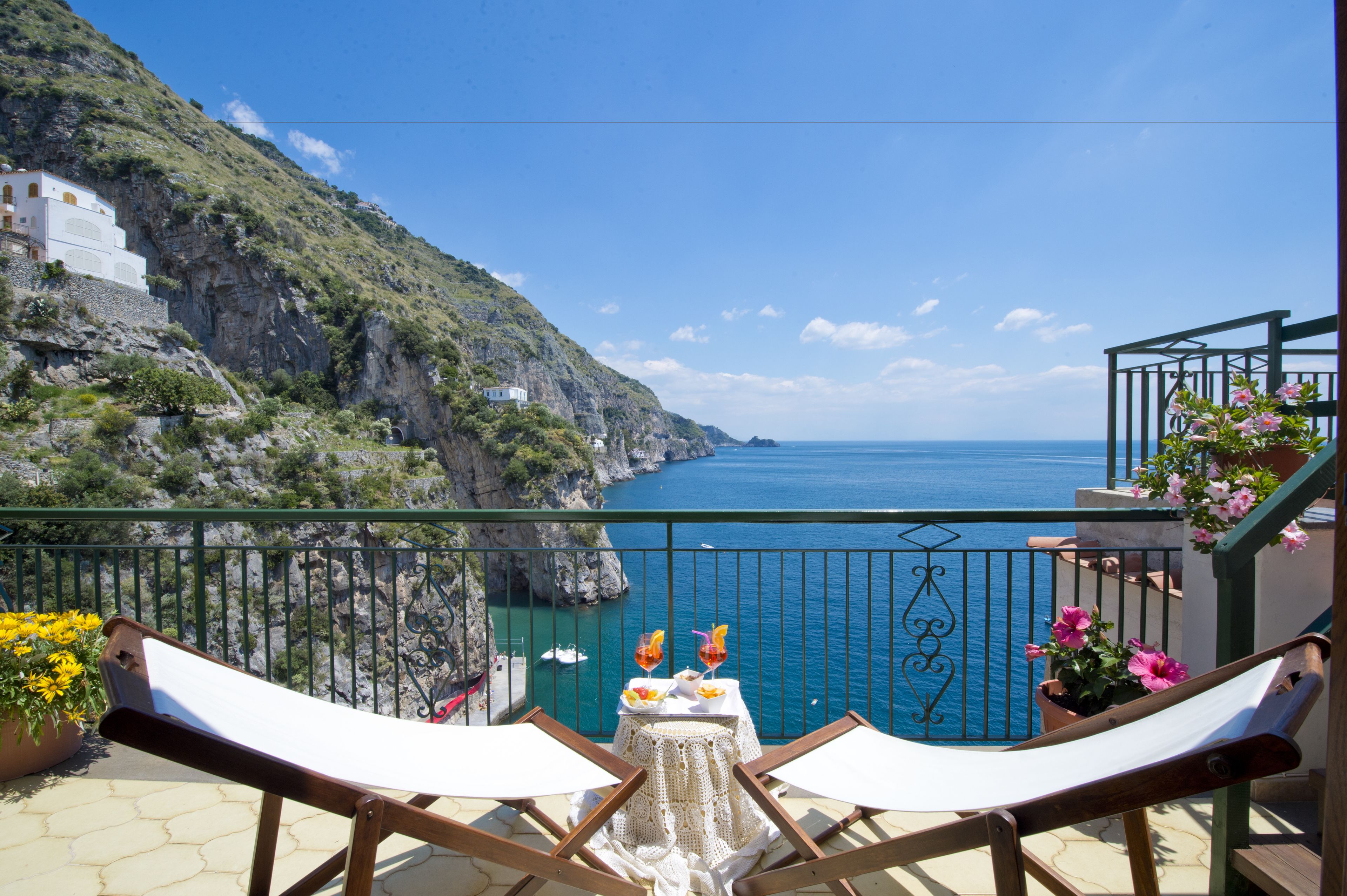 A balcony with a view of the sea, a table with drinks, and flowers.